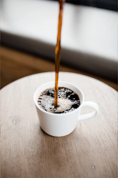 Someone pouring coffee into a cup on a wooden table
