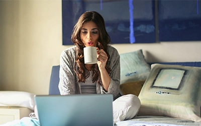 Picture of a girl who drinking a hot coffee while working on her laptop.
